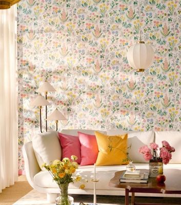 Den färgglada tapeten Aurora av Josef Frank för Svenskt Tenn matchas med rosa och gula inredningsdetaljer i ett ljust vardagsrum.